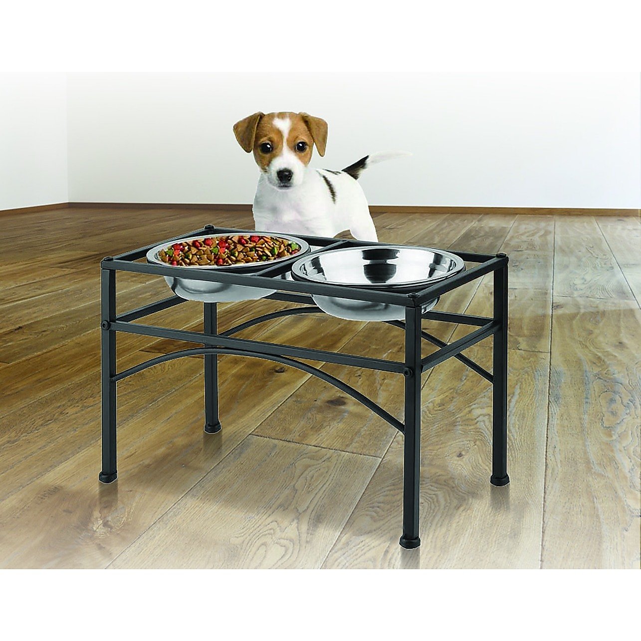 Dog standing next to a raised pet feeder with food on a wooden floor.