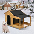 Wooden doghouse with a black roof in a snowy landscape with a white dog sitting outside.
