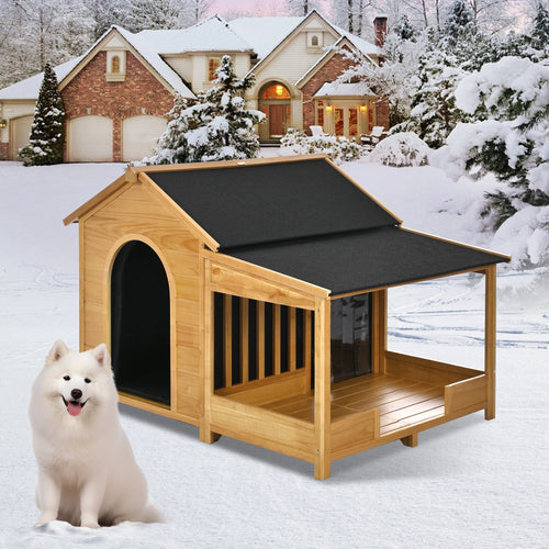 Wooden doghouse with a black roof in a snowy landscape with a white dog sitting outside.